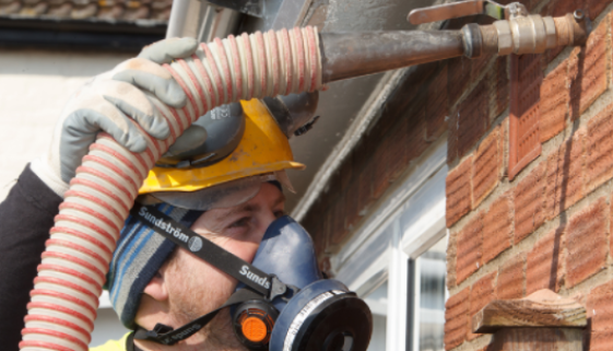 Technician installing cavity wall insulation into a brick house using specialist equipment.
